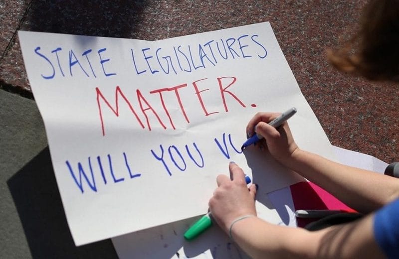 A woman writes "State legislatures matter. Will you vote?" on a paper sign