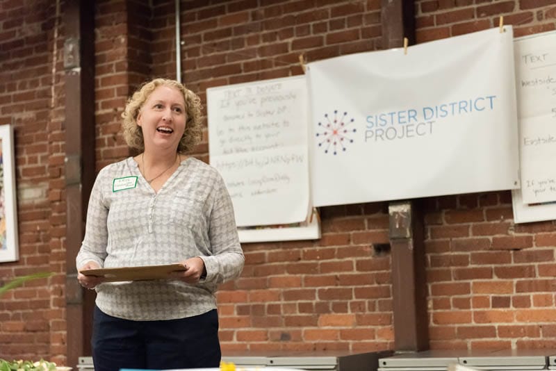 Volunteer in portland speaks in front of a Sister District banner