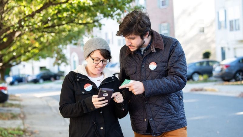 Two young people walking down the street looking at a phone while canvassing