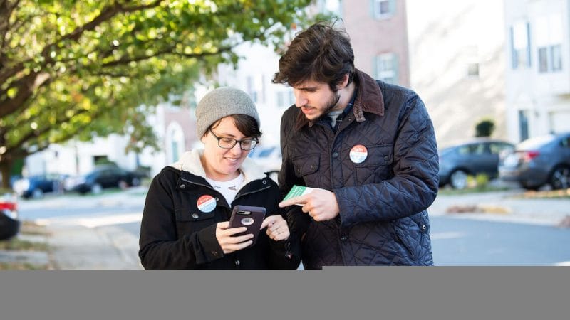 Two young people walking down the street looking at a phone while canvassing