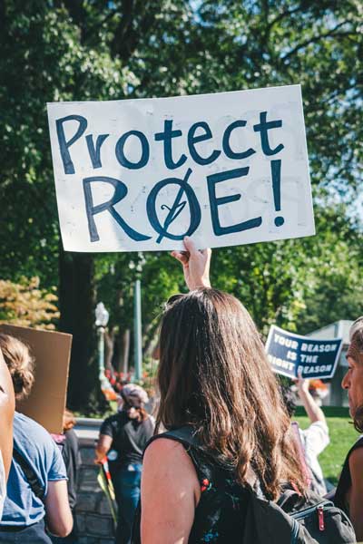 Girl at protest for reproductive rights holds a sign that says "Protect Roe" with a hanger crossed out